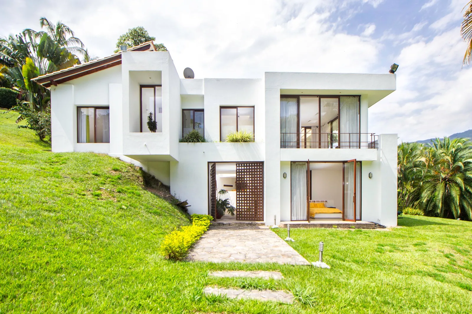 Casa blanca de dos pisos en una ladera con pasto